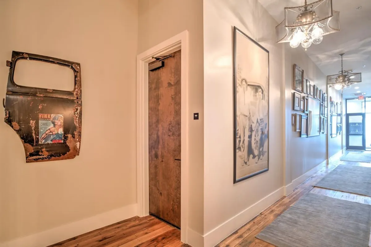 This image captures a hallway adorned with vintage and eclectic artwork, including a rusty car door mounted on the wall, a large framed photograph, and an array of smaller framed pictures. The decor evokes a nostalgic, artistic mood and invites curiosity and conversation, echoing Asheville’s creative spirit.