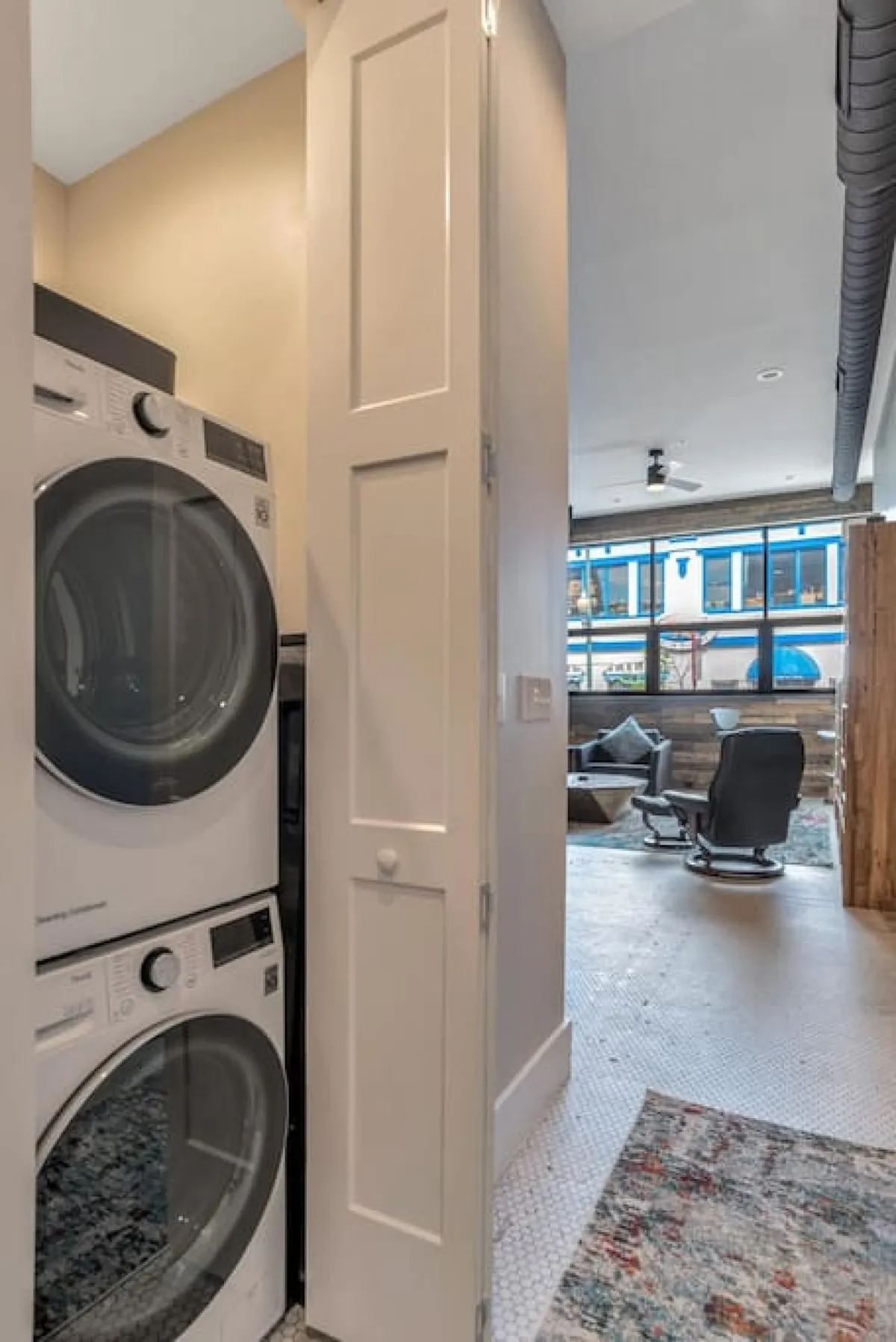 This image shows a tidy laundry area featuring a washer and dryer, a textured rug, and a door opening into the main living space. The setting is functional and welcoming, emphasizing ease of access between spaces.